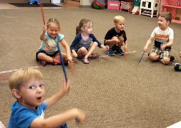 Kids playing rhythm sticks in a circle during class